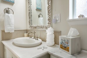 A bathroom with a round sink, a mirror with a stone frame, a towel rack, and a tissue box.