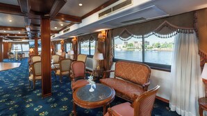 A luxurious cabin with a large window offering a view of the water, plush seating, and a well-lit interior. - Orient Nile Romance Nile Cruise - Every Saturday from Luxor for 07 & 04 Nights - Every Wednesday From Aswan for 03 Nights (Luxor)