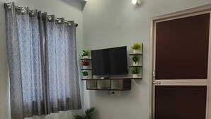 Un dormitorio con cama, televisión montada en la pared, armario y ventana con cortinas.
