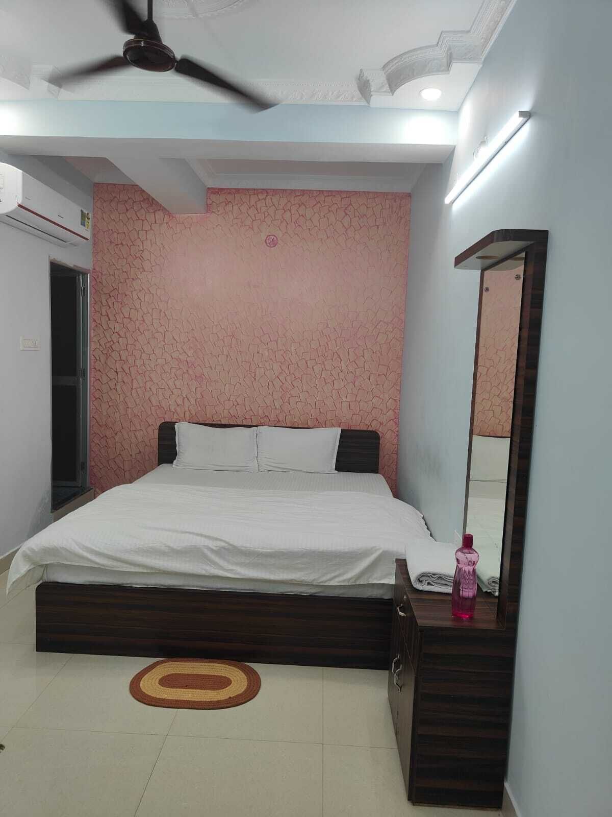 A bedroom with a bed, a ceiling fan, a mirror, and a small table with a bottle.