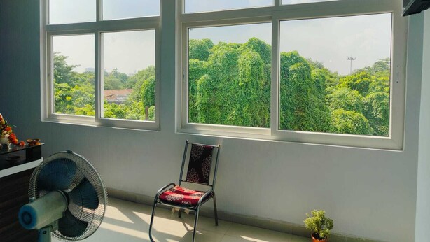 Una habitación con ventanas amplias, una silla, un ventilador y una pequeña planta en maceta.