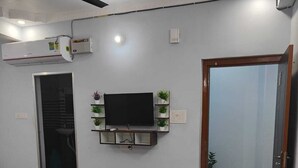Un dormitorio con cama, televisor montado, ventilador de techo y puerta que da a otra habitación.