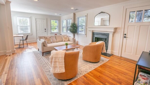 A spacious living room with hardwood flooring, a fireplace, a sofa, two armchairs, and a coffee table. - A Walk in the Pines - Bright & Cute 3br 2ba Home (North Charleston)