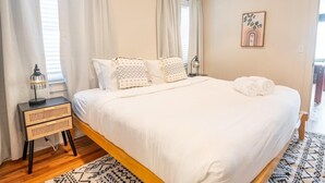 A neatly made bed with white linens and patterned pillows, a bedside table with a lamp, and a patterned rug. - A Walk in the Pines - Bright & Cute 3br 2ba Home (North Charleston)