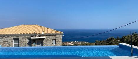 A swimming pool with a view of the sea and a stone building with a tiled roof.