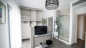 Un salon moderne avec un téléviseur posé sur un meuble, une cabine de douche en verre et une armoire blanche.