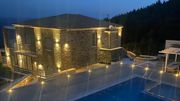 Une maison moderne dotée d’une piscine, d’une façade en pierre et d’un éclairage extérieur.