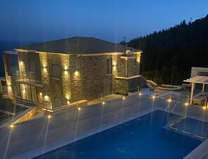 A modern house with a swimming pool, stone exterior, and outdoor lighting. - Tsapelas Villas (Ikaria)