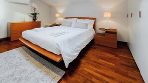 Um quarto moderno com uma cama grande, mesas de cabeceira de madeira, um aparador e uma mesa de cabeceira com luminárias.
