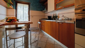 Uma cozinha com armários de madeira, forno de aço inoxidável e área de refeições com uma cadeira e uma fruteira.