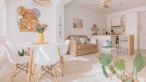 Una sala de estar moderna con una mesa de comedor blanca, un sofá color beige y una cocina con barra.