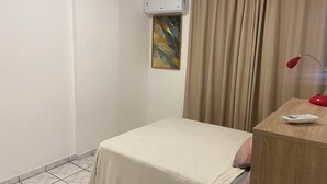 Une petite chambre à coucher, bien rangée, avec un lit simple, une table de chevet avec une lampe et un appareil de climatisation fixé au mur.