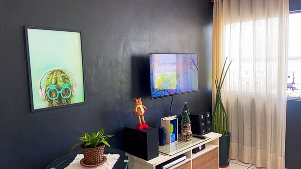 Un salon moderne avec un téléviseur à écran plat fixé au mur, une petite figurine d’ours posée sur un haut-parleur, une plante en pot et un sapin de Noël sur une étagère.