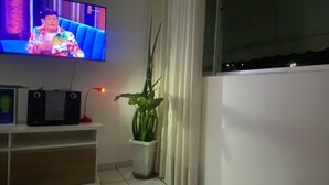Un téléviseur fixé au mur, une plante dans un pot blanc et une étagère avec des appareils électroniques.