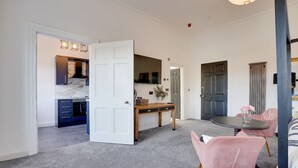 A spacious room with a large open door leading to a kitchen, a dining area with pink chairs, and a black table. - No 2 @ The Rocket Rooms Apartments  (Berwick-upon-Tweed)
