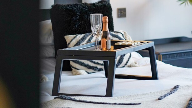 A neatly made bed with a black and white striped pillow, a small table with a bottle and glasses, and a lamp in the background. - No 2 @ The Rocket Rooms Apartments  (Berwick-upon-Tweed)