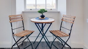 A small room with a window, two wooden chairs, a round table with a plant, and a view of a building. - No 2 @ The Rocket Rooms Apartments  (Berwick-upon-Tweed)