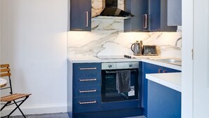 A modern kitchen with dark blue cabinets, a marble countertop, a built-in oven, and a pendant light fixture. - No 2 @ The Rocket Rooms Apartments  (Berwick-upon-Tweed)