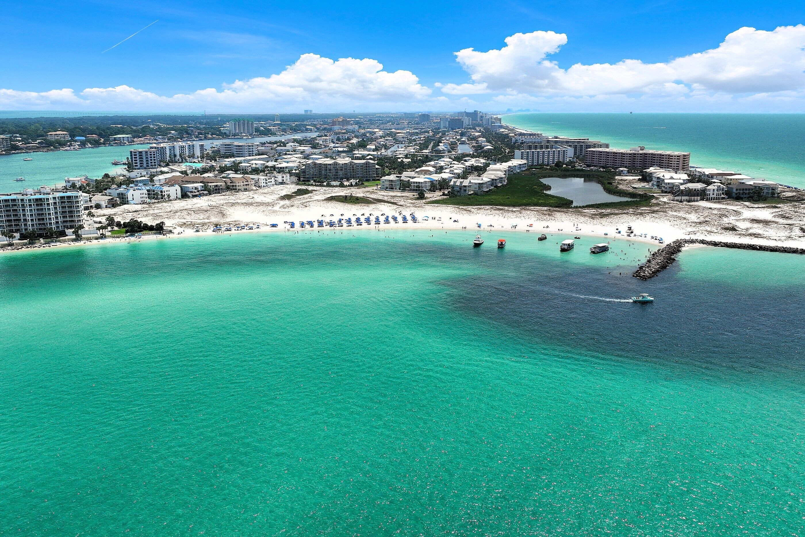 Vista aérea de un resort costero con playa, aguas turquesas cristalinas y un puerto deportivo.