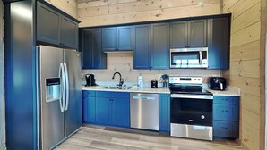 A modern kitchen with stainless steel appliances, blue cabinets, and a wooden ceiling.