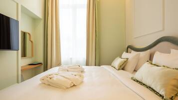 Een net opgemaakt bed met witte lakens en groene accenten, een nachtkastje met een boek, en een groot raam met gordijnen.