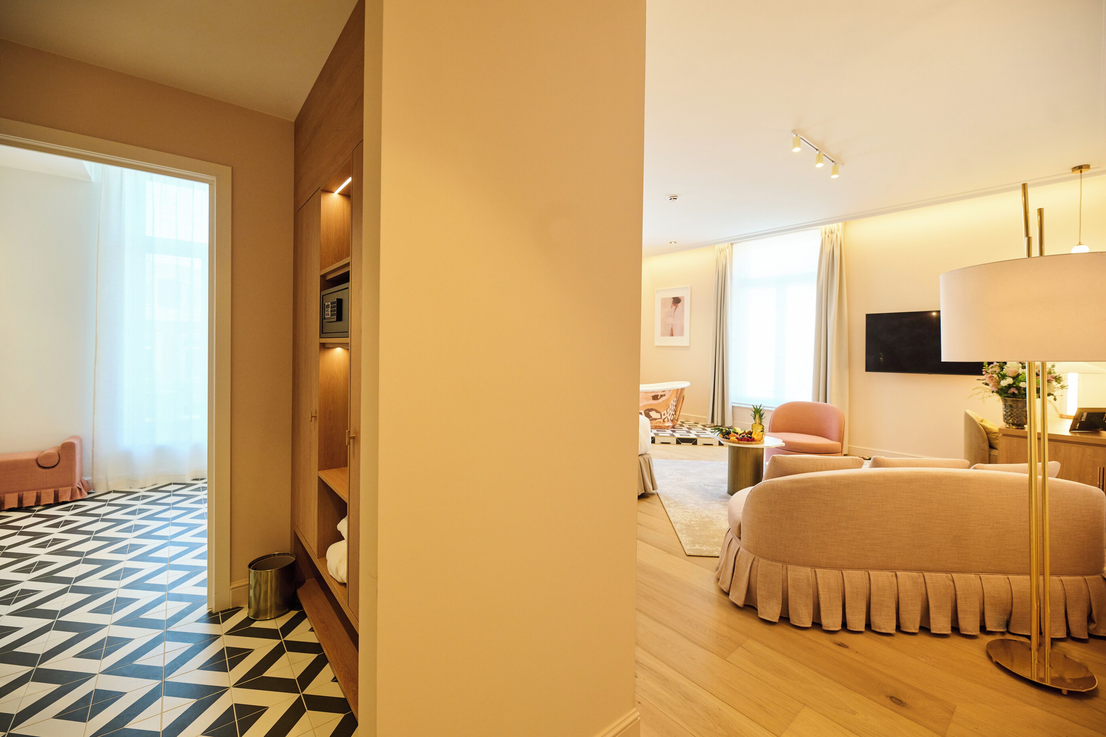 Una habitación de hotel moderna con piso de diseño geométrico, una cama redonda grande, un armario de madera, una mesita de noche con lámpara y un televisor en la pared.