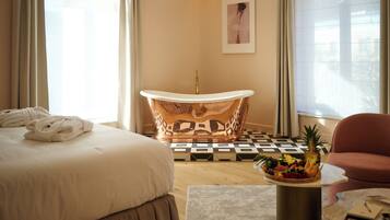 Habitación de hotel con una cama grande, una bañera, un frutero y una silla.