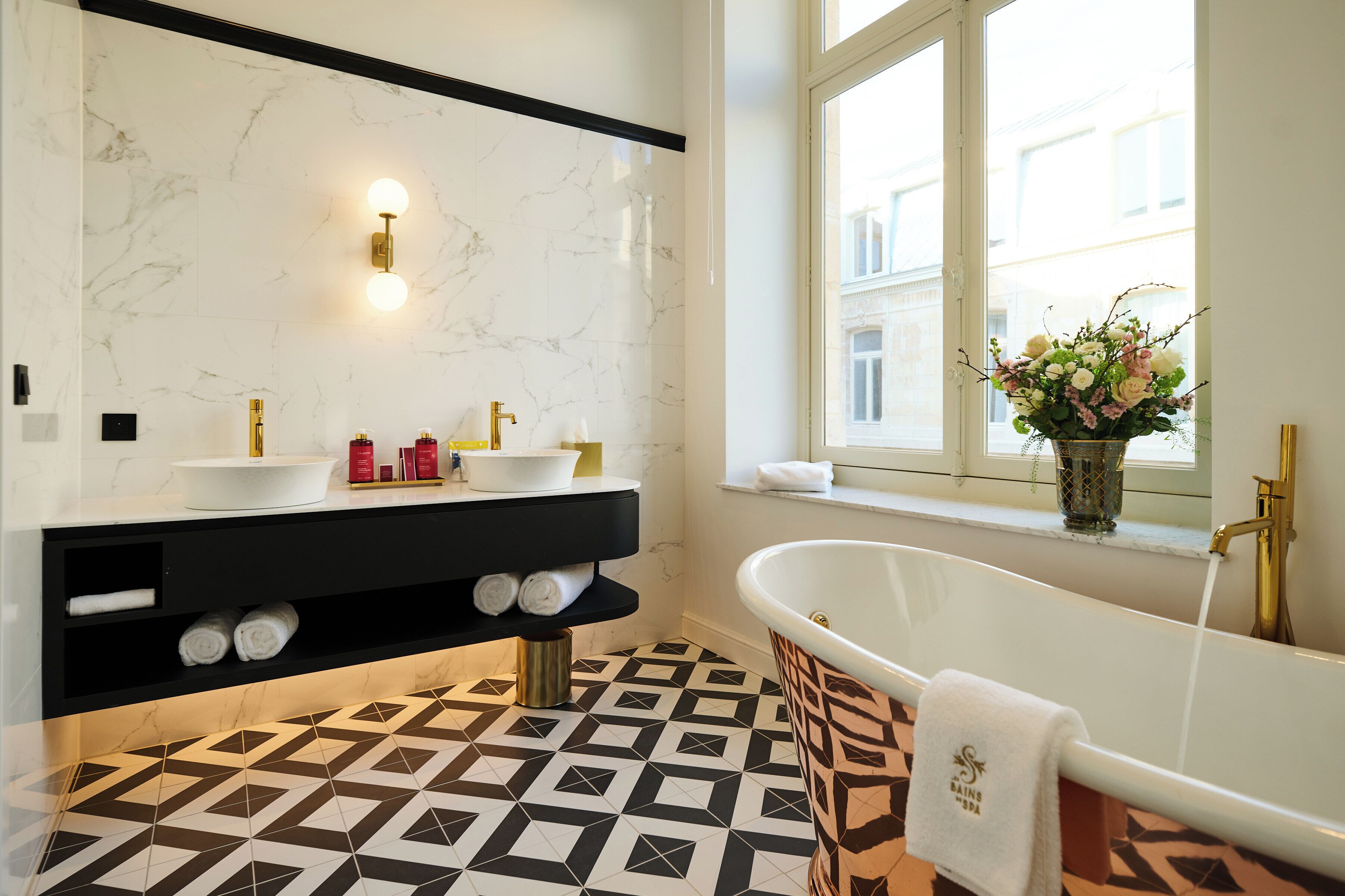 Un baño moderno con una bañera independiente, un tocador negro con lavamanos blanco y un suelo con estampado geométrico.