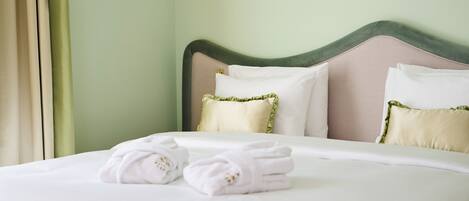 A neatly made bed with white linens, two pillows, and a pair of folded towels.