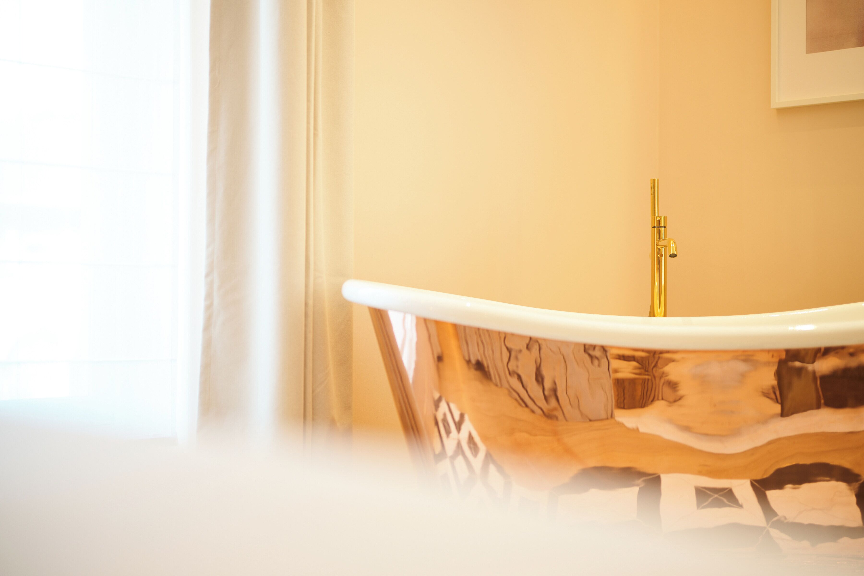 A bathroom with a bathtub, a gold faucet, and a framed picture on the wall.