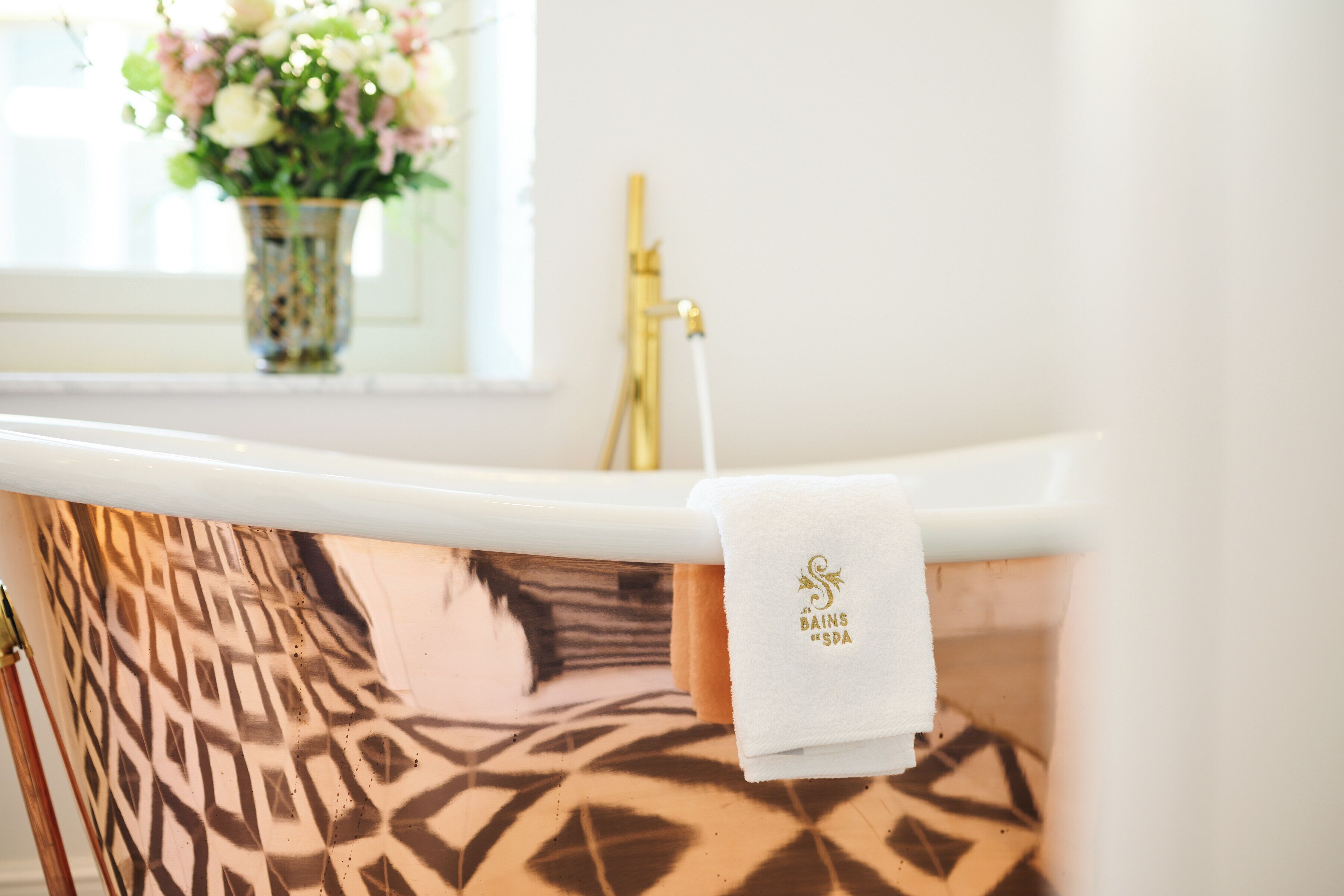 Une salle de bain avec une zone de douche aux motifs décoratifs, une baignoire blanche et une serviette suspendue au bord de la baignoire.