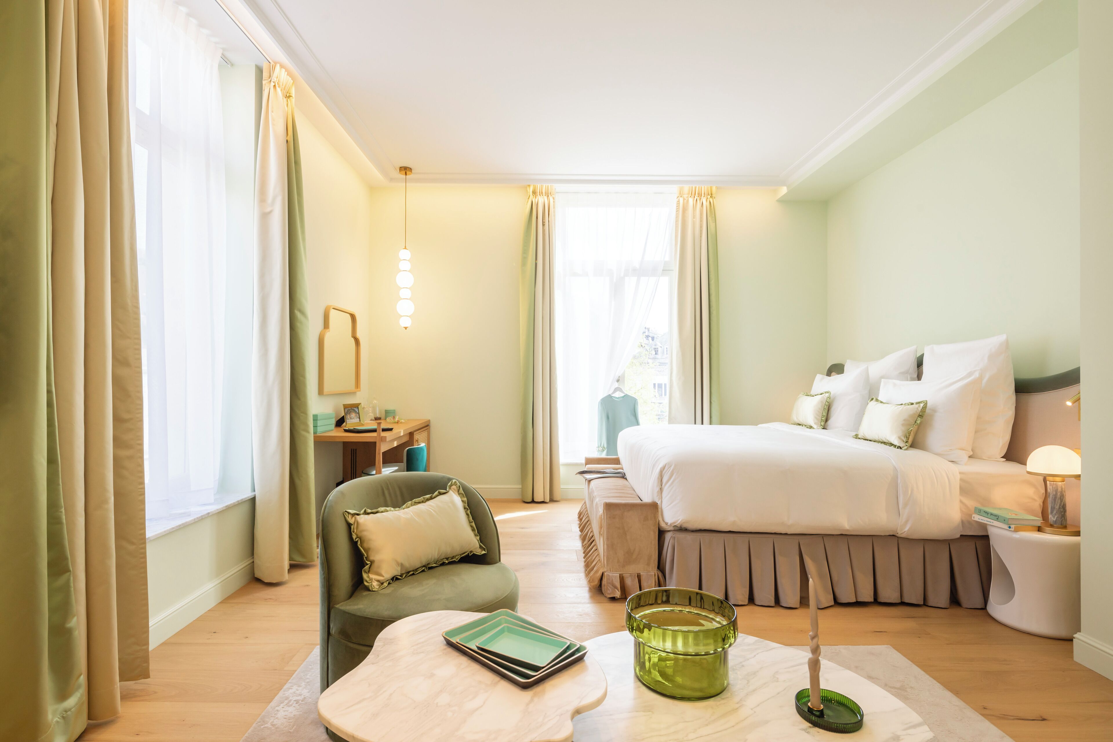 A hotel room with a bed, a chair, a bedside table, a lamp, and a window with curtains.