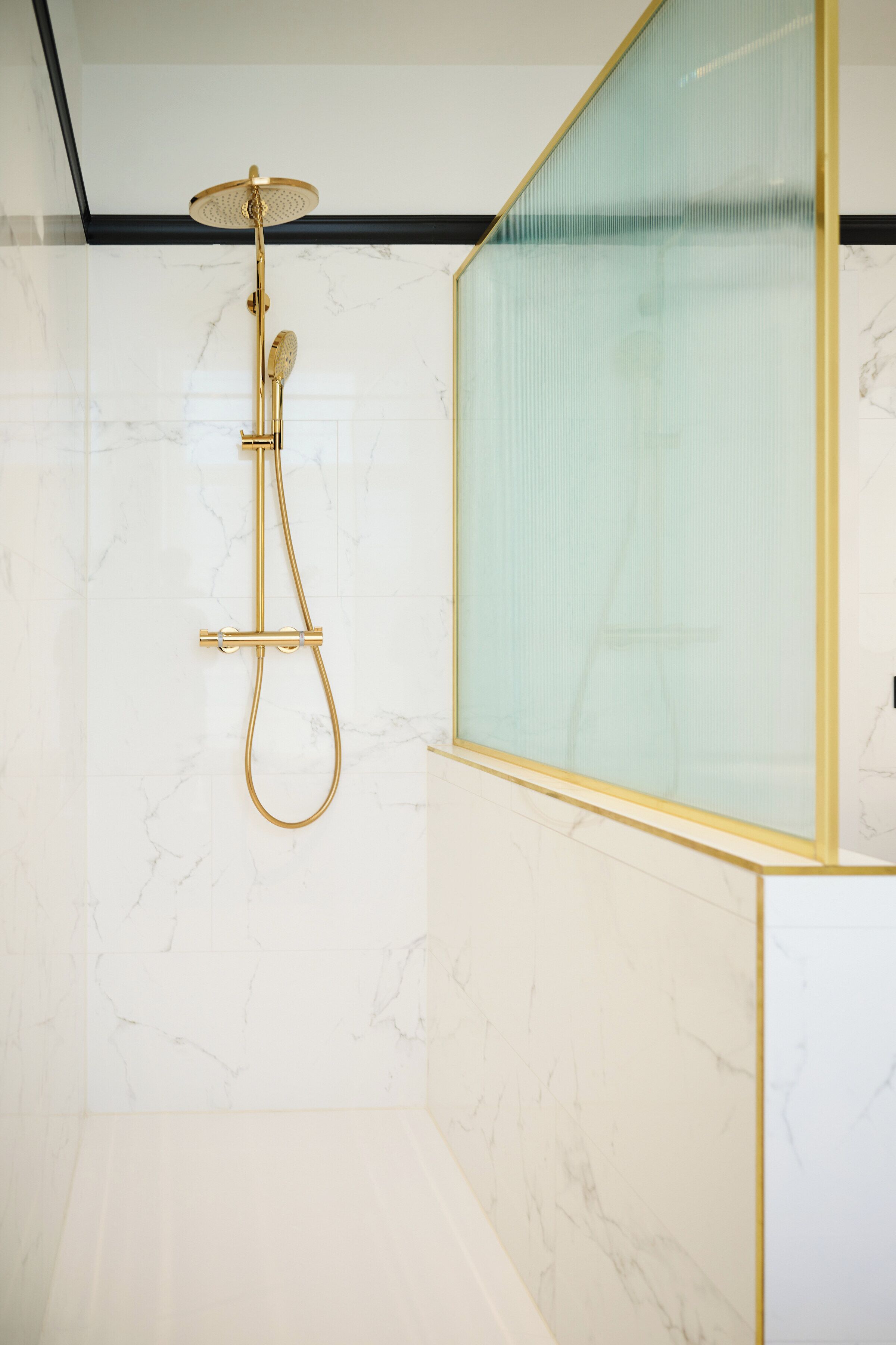 A modern bathroom with a gold showerhead and a glass partition.