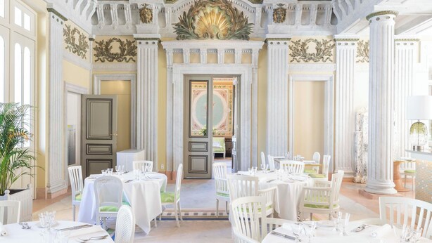 A grand hall with ornate ceiling frescoes, classical columns, and a symmetrical layout with tables set for dining. - Les Bains De Spa (Spa)