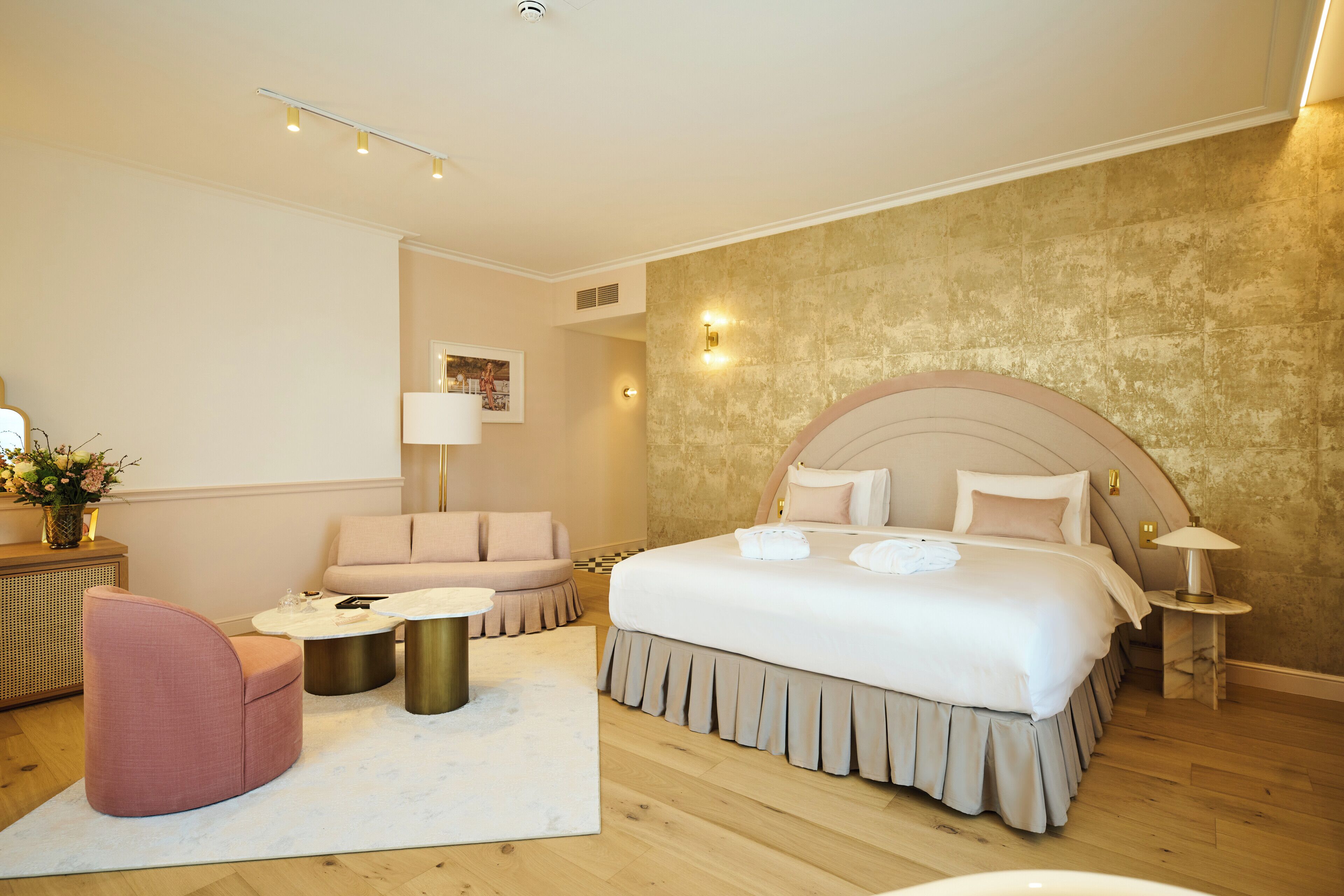 A modern hotel room with a large bed, a sofa, a round coffee table, and a small side table.