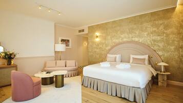 Una habitación de hotel moderna con una cama grande, un sofá, una mesita redonda y una mesita auxiliar pequeña.