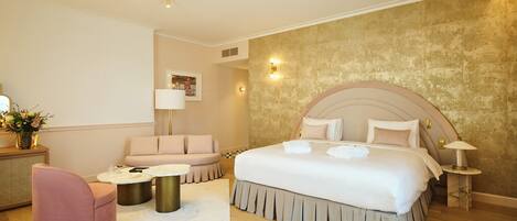 A modern hotel room with a large bed, a sofa, a round coffee table, and a small side table.