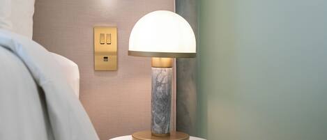 A bedside table with a lamp, a wall socket, and a marble-like base.