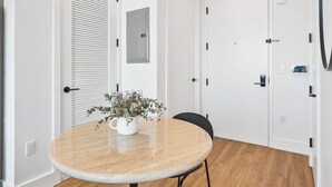 A modern, minimalist dining area with a round table, black chairs, and a potted plant.
