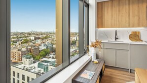 A modern kitchen with large windows, a wooden cabinet, and a view of a cityscape.