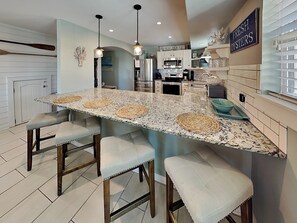 A kitchen with a central island, bar stools, a refrigerator, and a sign indicating fresh oysters.