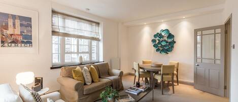 A modern living room with a beige sofa, a coffee table, and a dining area with chairs.