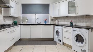 Eine moderne Küche mit weißen Schränken, einer integrierten Waschmaschine und einer grauen Fliesenrückwand.