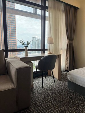 Ein Hotelzimmer mit großem Fenster, Schreibtisch, Stuhl, Bett und einer Sitzecke.