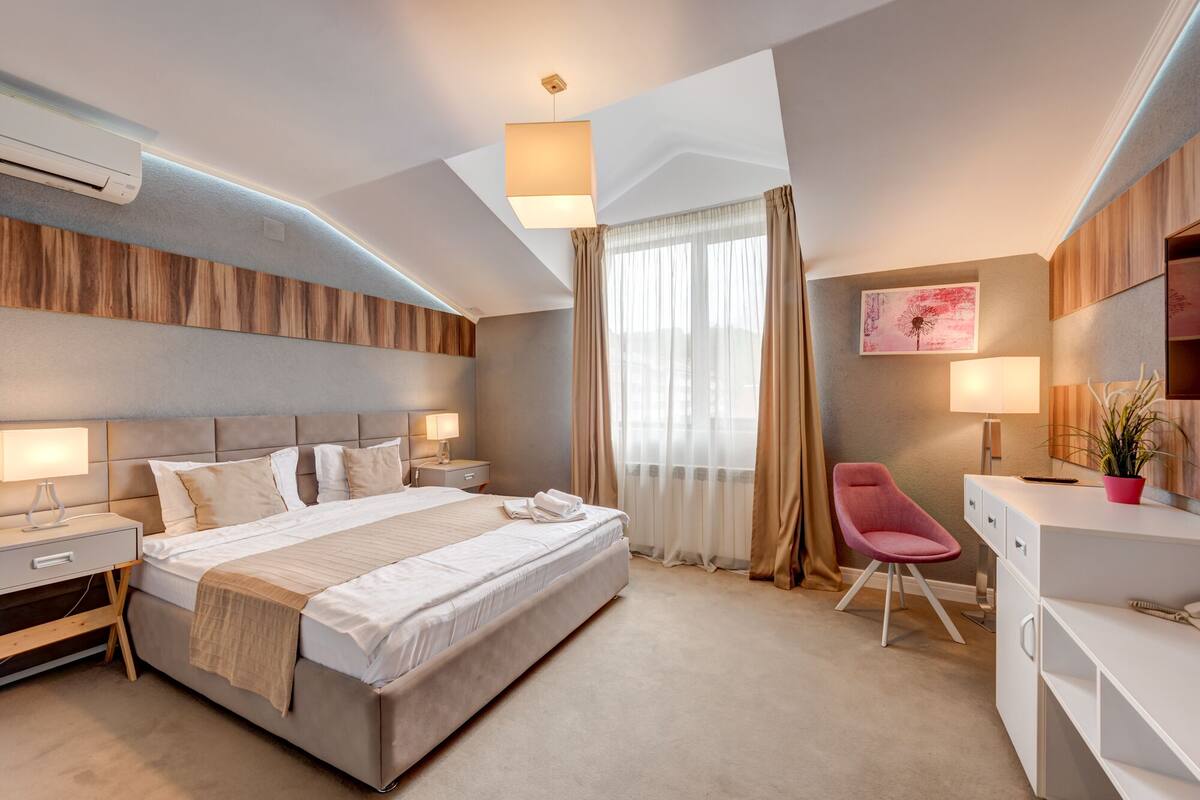 Une chambre d’hôtel moderne avec un grand lit, des tables de chevet avec des lampes, un bureau, une chaise et une plante en pot.