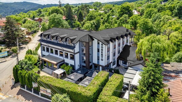 Een modern hotel met een tweelaags gebouw, een overdekt buitengebied en uitzicht op de omliggende begroeiing en heuvels.