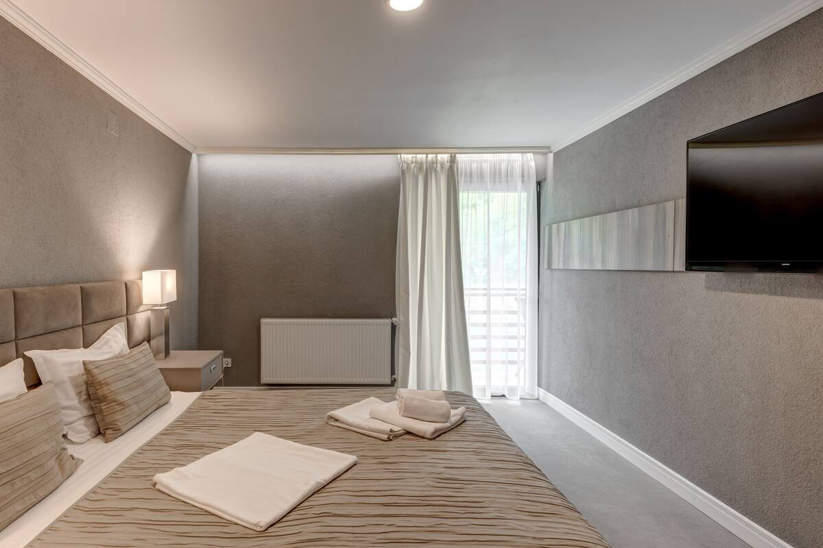 Une chambre à coucher moderne avec un grand lit, une table de chevet avec une lampe, un radiateur et un téléviseur fixé au mur.