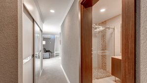Een moderne hotelgang met een houten deur die leidt naar een badkamer met douche en wastafel.