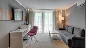 Een moderne hotelkamer met een grijze bank, een witte tafeltje, een rode stoel, een bureau met telefoon en een groot raam met gordijnen.