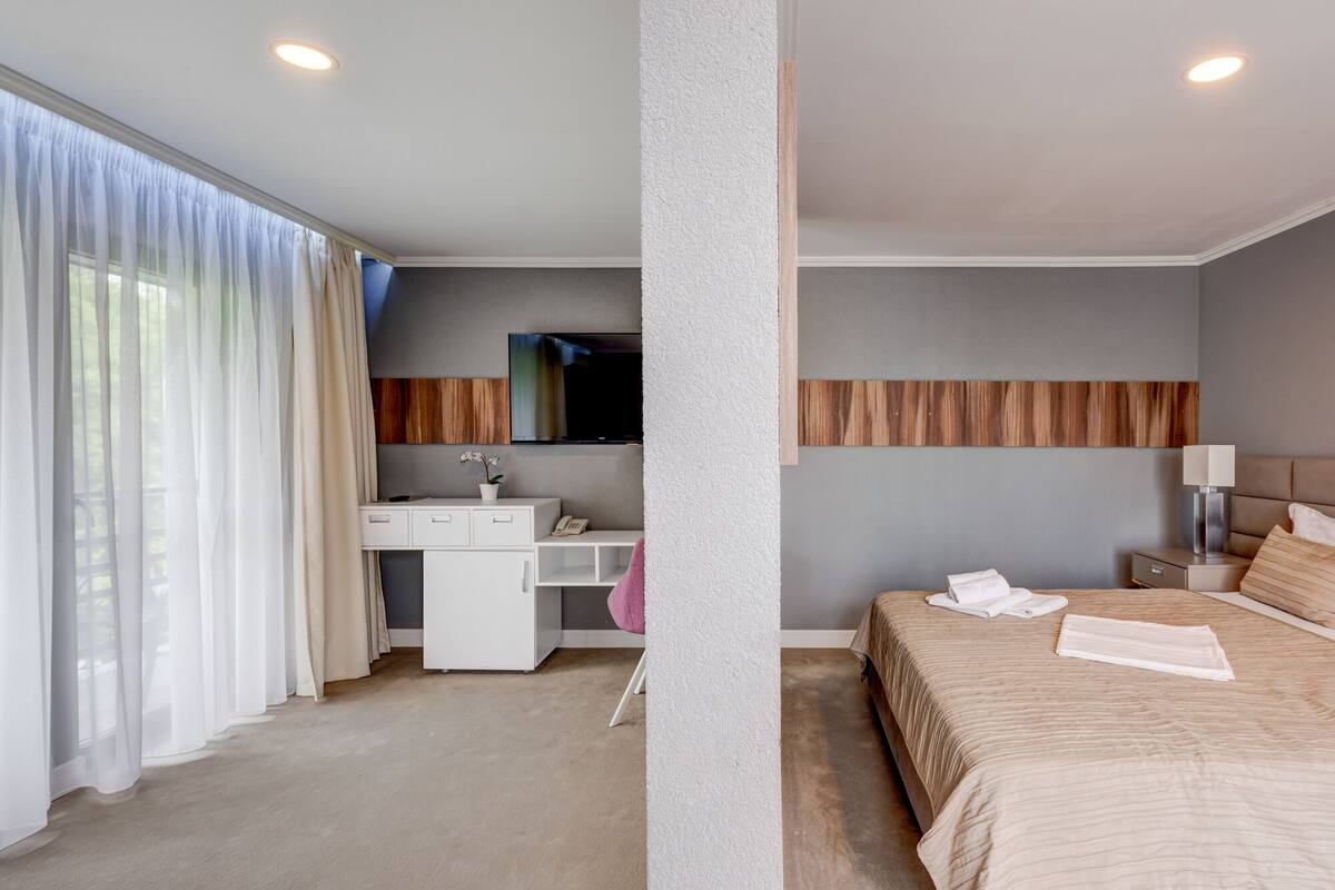 Une chambre d’hôtel avec un lit, un bureau avec un téléphone, une télévision et une grande fenêtre avec des rideaux.